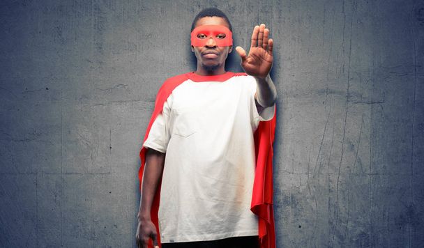 Afrikanischer schwarzer Superheldenmann ärgert sich über schlechte Haltung, indem er Stoppschild mit der Hand macht, Nein sagt, Sicherheit, Verteidigung oder Beschränkung ausdrückt, vielleicht schiebt - Foto, Bild
