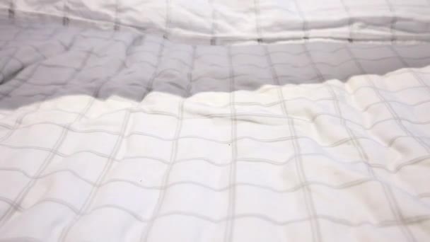 Witte lakens met grijze strepen zijn gegooid en gooide, zwevende neer op een bed - Video