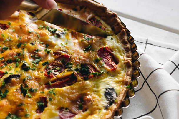 męskiej ręki cięcia pyszne pizze z serem, pomidorami i zioła, tradycyjne dania kuchni włoskiej  - Zdjęcie, obraz