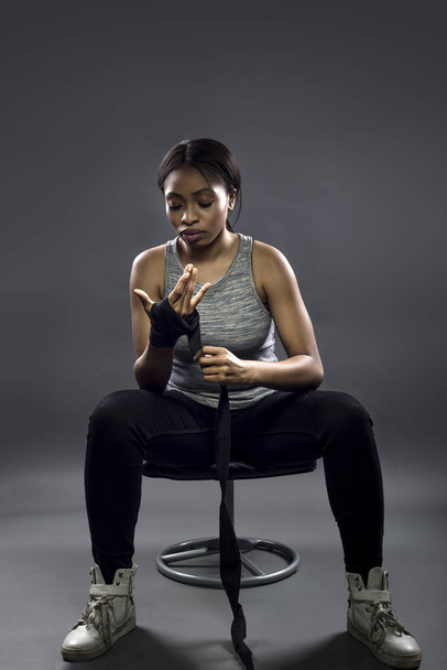Black female fighter or boxer preparing by wearing gloves and wrapping wrist.  She is dressed in a modest athletic outfit.  The image depicts self defense and sports. - Fotó, kép