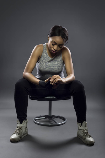 Black female fighter or boxer preparing by wearing gloves and wrapping wrist.  She is dressed in a modest athletic outfit.  The image depicts self defense and sports. - Foto, Imagen