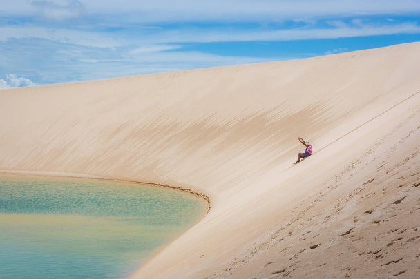 Mulher se divertindo, rolando uma enorme duna de areia em um cenário incrível, lagoa de piscina natural no fundo. Norte do Brasil, América do Sul
. - Foto, Imagem