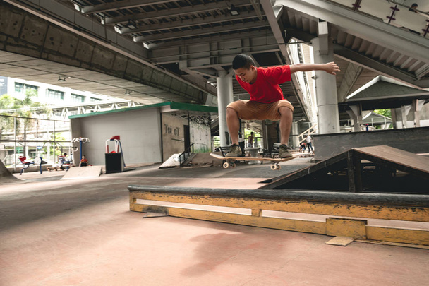 Skateboarder in action. Asian boy in urban skateboard park under the bridge doing trick. Natural light setting. - Photo, Image