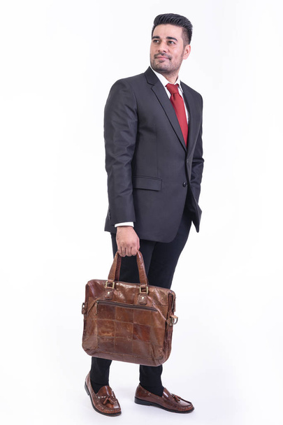 Businessman isolated in white background. Handsome young indian businessman in suit with bag portrait, hands in pocket looks. Full length shot. - Foto, immagini