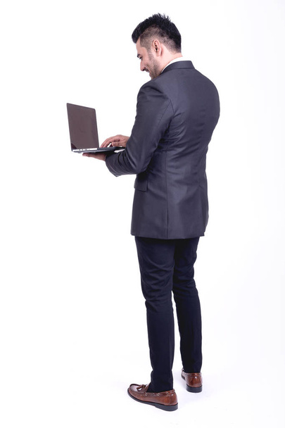 Businessman isolated. Handsome young indian businessman in suit with laptop portrait, confident smile looks. Full length shot. - Valokuva, kuva