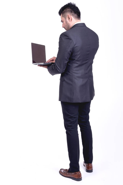 Businessman isolated. Handsome young indian businessman in suit with laptop portrait, focus looks. Full length shot. - Fotó, kép