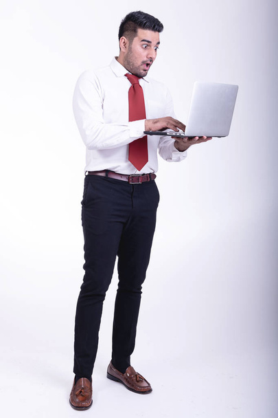 Businessman isolated. Handsome young indian businessman using laptop portrait, shocking looks. Full length shot. - Fotografie, Obrázek