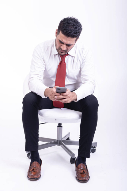 Businessman sitting on white chair isolated. Handsome young indian businessman using mobile phone, very focus looks.  Full length shot. - Fotoğraf, Görsel