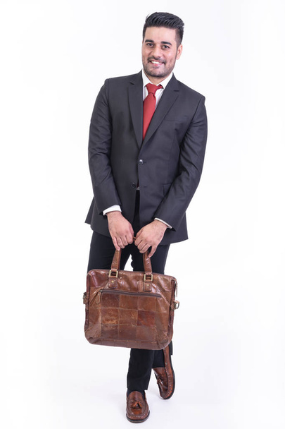 Businessman isolated in white background. Handsome young indian businessman in suit with bag portrait, bag in front smile looks. Full length shot. - Foto, Imagem