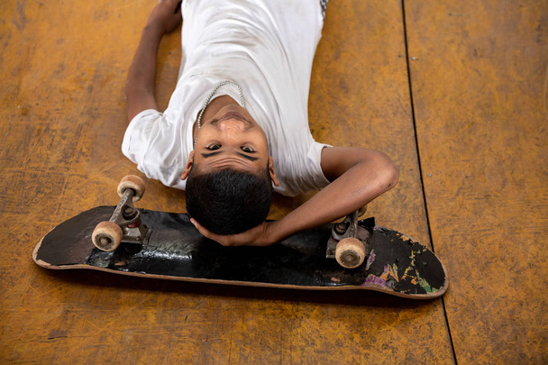 Skateboarder portrait. Smiling Asian boy in urban skateboard park under the bridge laying on  dirty ramp. Natural light setting. - Fotografie, Obrázek