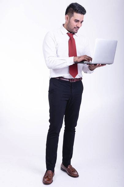 Businessman isolated. Handsome young indian businessman using laptop portrait, confident looks. Full length shot. - Foto, imagen