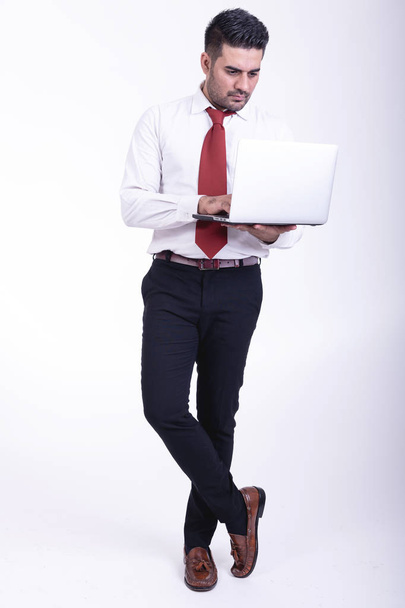Businessman isolated. Handsome young indian businessman using laptop portrait, confident looks. Full length shot. - Photo, Image