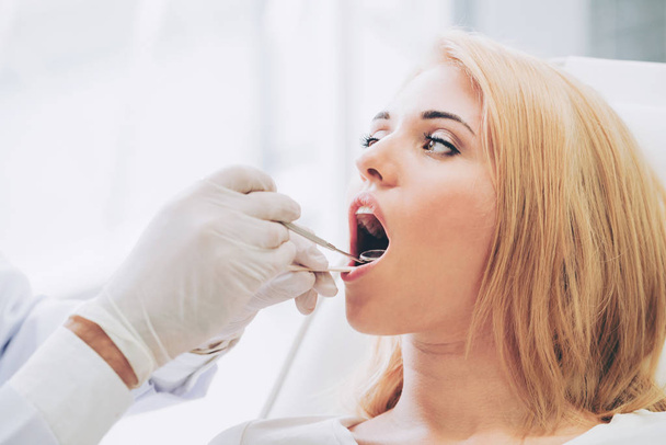 Jovem dentista bonito examinando dentes de mulher feliz paciente sentado na cadeira de dentista na clínica odontológica. Conceito de assistência odontológica
. - Foto, Imagem