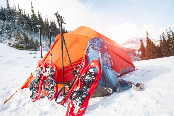 Schneeschuhe, Rucksack und Wanderstöcke in der Nähe des Zeltes. Ausrüstung für eine Winterwanderung vor dem Hintergrund von Wald und Bergen. Zelten in den Bergen. Winteraufstieg. - Foto, Bild