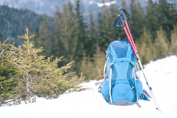 Rucksack vor dem Hintergrund schneebedeckter Berge und blauen Himmels. Ein Rucksack im Schnee. Aktiver Lebensstil. Wandern im Winter. Ausrüstung zum Wandern. Trekkingstöcke. - Foto, Bild