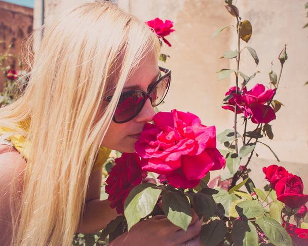 Bella donna annusa rose rosse profumate in giardino
 - Foto, immagini