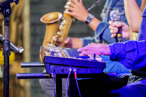 Nahaufnahme und Erntegruppe von Musikern, die ein elektronisches Keyboard, Saxophon und Gesang auf der Bühne spielen, mit blauem Licht auf verschwommenem Hintergrund. - Foto, Bild