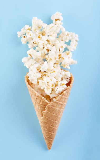 Popcorn w stożka wafel na lody na jasnym tle niebieski. Film. Fast food. Kukurydza - Zdjęcie, obraz