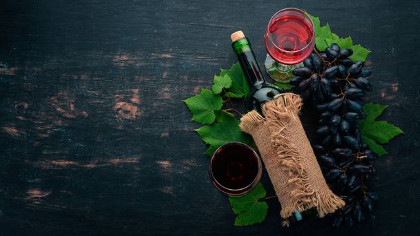 Red wine in a bottle with a glass and grapes. On a black wooden background. Free space for text. Top view. - Zdjęcie, obraz