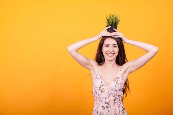Beautiful young woman holding pot with plant in studio over yellow background - Photo, Image