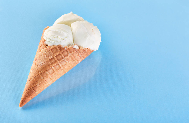 bolas de helado en un cono de gofre sobre un fondo azul. Helado de vainilla en un cono de gofre
. - Foto, imagen