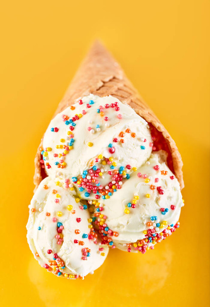 ijs ballen met gekleurde suiker hagelslag in een wafel kegel op een gele achtergrond. Vanille-ijs in een wafel kegel. - Foto, afbeelding