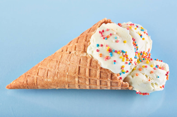 bolas de helado con azúcar de colores espolvorea en un cono de gofre sobre un fondo azul. Helado de vainilla en un cono de gofre
. - Foto, imagen