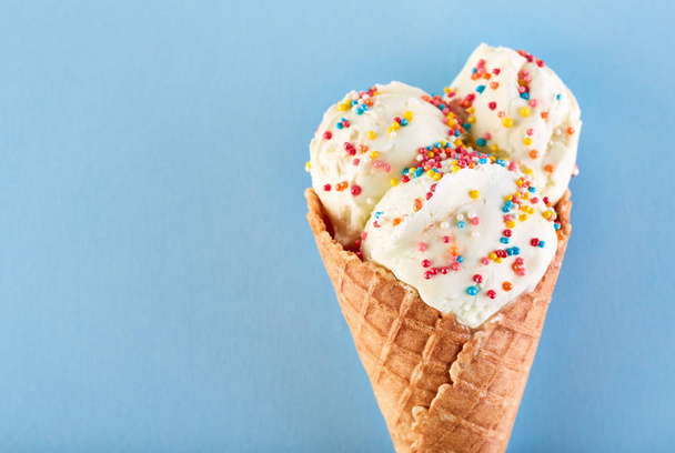 ice cream balls with colored sugar sprinkles in a Waffle Cone on a Blue Background. Vanilla ice cream in a waffle cone. - Φωτογραφία, εικόνα