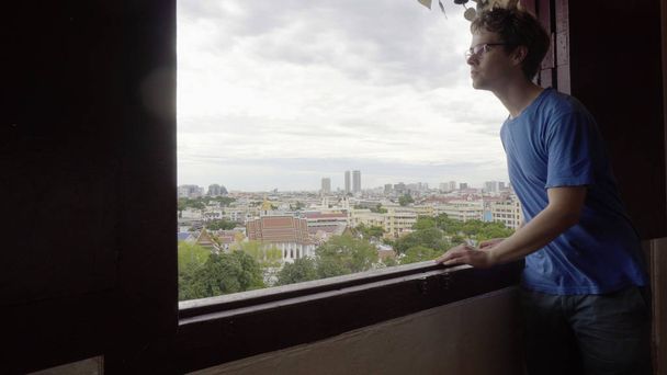 Молодой человек смотрит в окно с городом в фоновом режиме
 - Фото, изображение