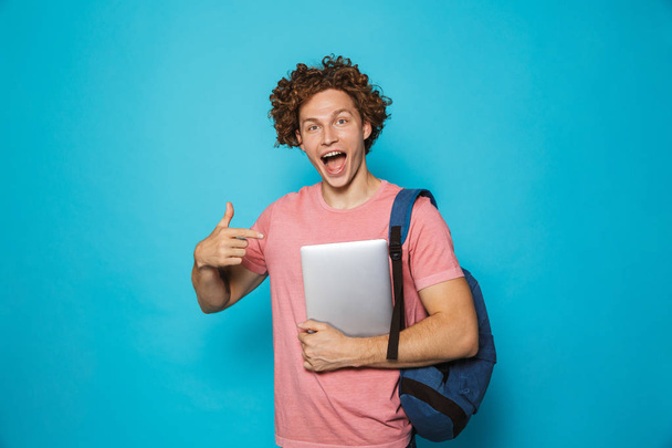 Image of caucasian youngster guy with curly hair wearing casual clothing and backpack holding laptop isolated over blue background - Photo, image