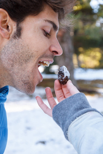 Novia alimentando una piña de un árbol a su novio bromeando en la nieve un día soleado
 - Foto, Imagen