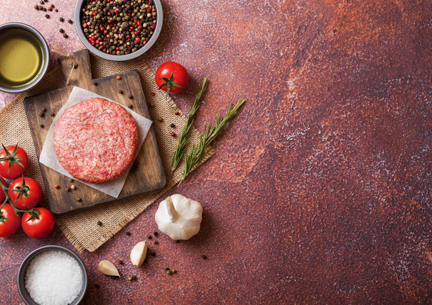 Raw minced homemade grill beef burger with spices and herbs. Top view and space for text. On top of chopping board and rusty  kitchen table background. With pepper salt and garlic. - Foto, imagen