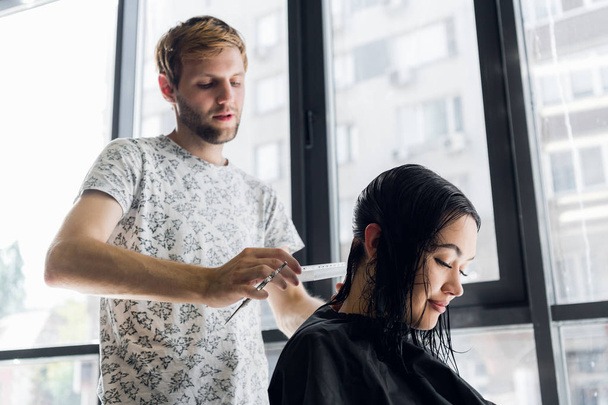 Młody profesjonalny Fryzjer męski hip cięcia ciemne włosy kobiety klienta w salonie. - Zdjęcie, obraz
