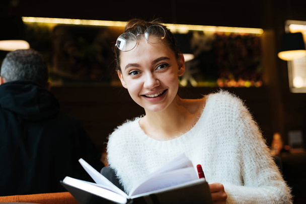 lachen van jong meisje student bril zitten in Cafe na studeren en lezen van boek - Foto, afbeelding