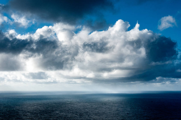 Em um belo dia ensolarado, nuvens cinzas, brancas e negras estão brincando sobre o mar e a chuva está caindo à distância
 - Foto, Imagem