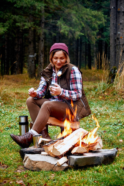 Wanderlust and Travel concept. Woman roast marshmallow candies on the campfire in forest. Spring or autumn camping - Foto, immagini
