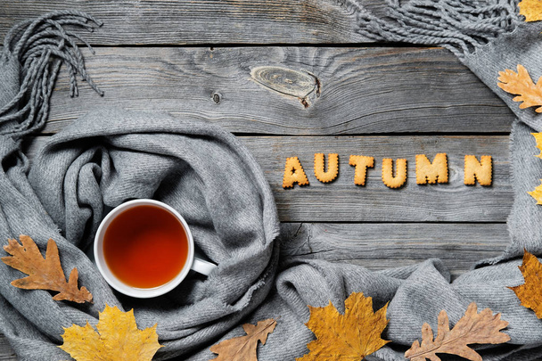 Autumn composition, fall leaves, hot steaming cup of tea and a warm scarf on wooden table background - Фото, изображение