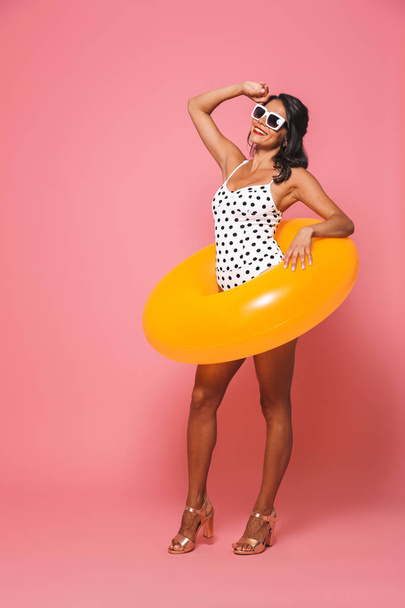 Picture of woman in swimwear posing isolated over pink wall background with beach rubber ring looking aside. - Φωτογραφία, εικόνα