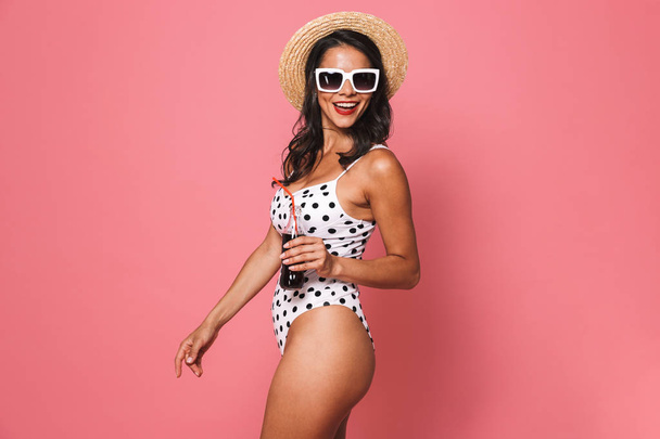 Image of pretty woman in swimwear posing isolated over pink wall background drinking soda looking aside. - Photo, Image