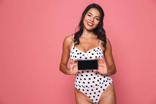 Photo of cheerful woman in swimwear posing isolated over pink wall background showing display of mobile phone. - Fotó, kép