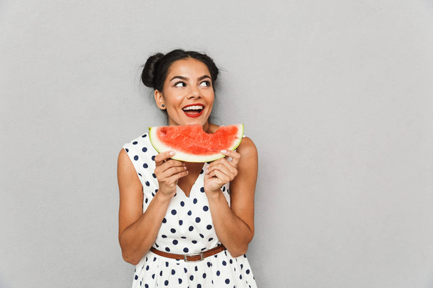 Portrait of a smiling young woman in summer dress isolated, holding watermelon slice - Foto, imagen
