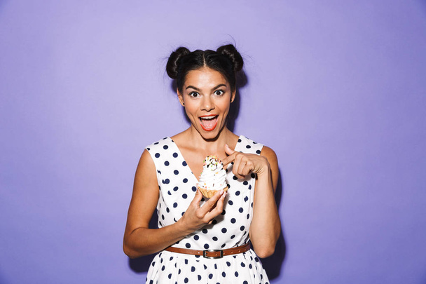 Portrait of an excited young woman in summer dress isolated, holding cupcake - Φωτογραφία, εικόνα