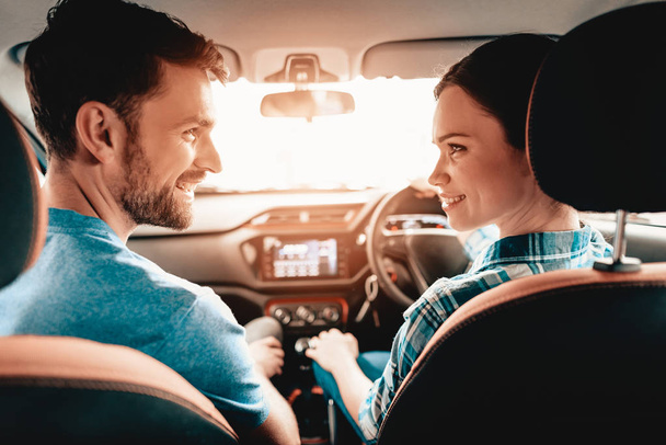 Smiling Couple Sitting In A Frontseat Of A New Car. Young Family. Automobile Salon. Cheerful Driver. Successful Buying. Good Mood. Great Trade. Sunny Windshield. Look At Each Other. - 写真・画像