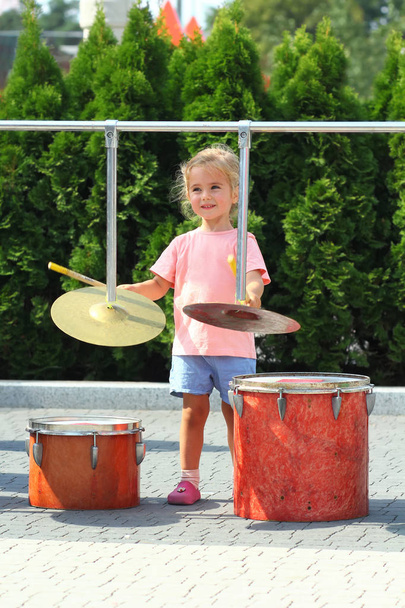Двухлетняя симпатичная девочка учится играть в барабаны на открытом воздухе
 - Фото, изображение