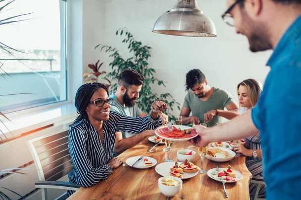 Gruppe fröhlicher junger Freunde, die zu Hause zu Abend essen. Gruppe multiethnischer Freunde genießt Dinnerparty - Foto, Bild