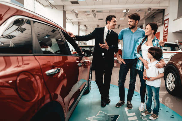 Happy Young Family Are Choosing A New Car In Showroom. Dialogue With Dealer. Cheerful Customer. Auto Rewiew. Make A Decision. End Of A Deal. Good Offer. Buyer And Seller. Business Trade. - Fotografie, Obrázek
