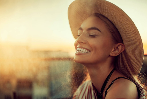 Retrato de mujer feliz joven en sombrero contra de fondo urbano al atardecer. Retroiluminación
. - Foto, imagen