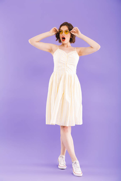 Full length portrait of an excited young woman dressed in summer clothes posing while standing and looking away over violet background - Foto, imagen