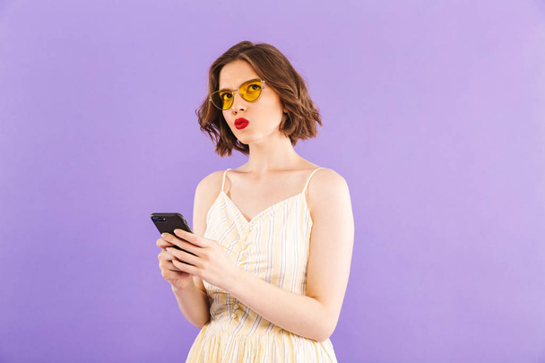 Photo of thoughtful young woman using mobile phone isolated over purple wall background. - Foto, Imagem