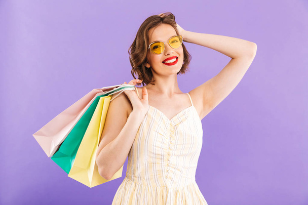 Photo of excited emotional young woman isolated over purple wall background holding shopping bags. - Photo, Image